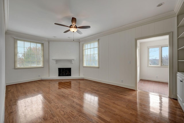 unfurnished living room with ornamental molding, a brick fireplace, ceiling fan, and light hardwood / wood-style floors