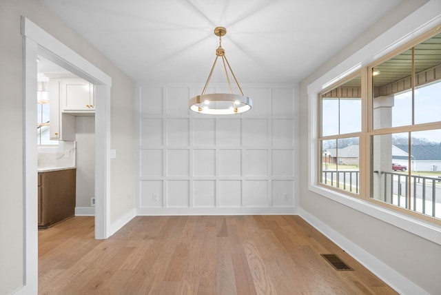 unfurnished dining area with a notable chandelier, a decorative wall, visible vents, baseboards, and light wood finished floors