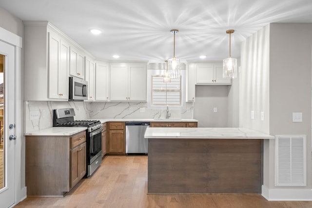 kitchen with light stone counters, stainless steel appliances, visible vents, white cabinets, and a sink