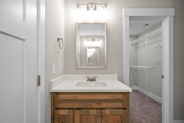 bathroom with a walk in closet, vanity, and baseboards