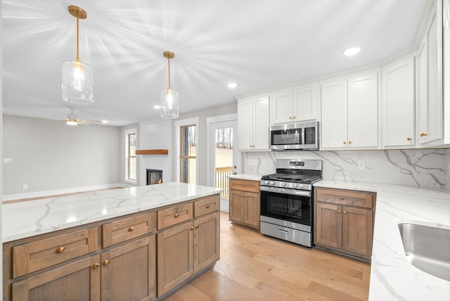 kitchen with stainless steel appliances, white cabinets, open floor plan, brown cabinetry, and decorative light fixtures