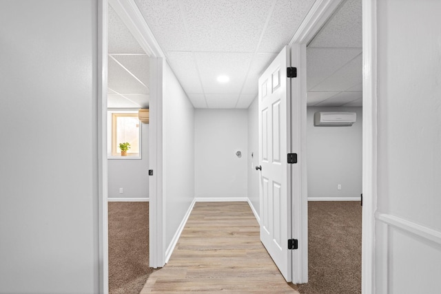 hall with a drop ceiling, light colored carpet, and an AC wall unit