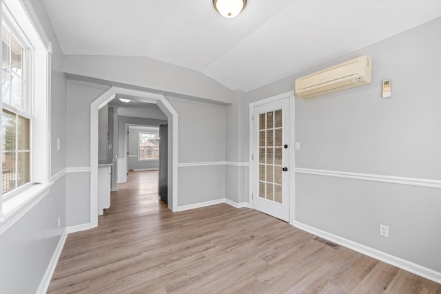 interior space with lofted ceiling, a wall mounted air conditioner, and light hardwood / wood-style flooring