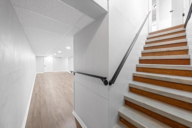 stairs featuring wood-type flooring and a drop ceiling