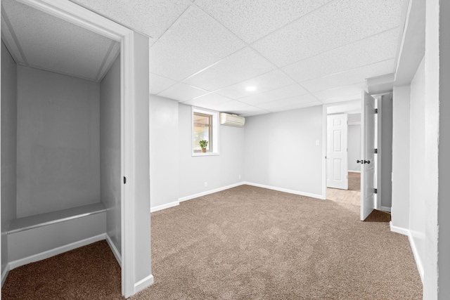 basement with a drop ceiling, an AC wall unit, and carpet