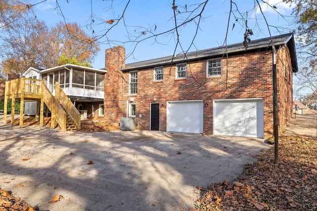 rear view of property featuring a garage, a wooden deck, a sunroom, and central AC unit