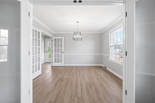 unfurnished dining area featuring crown molding, a chandelier, light wood-type flooring, and french doors