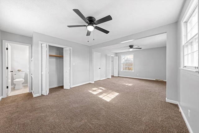 unfurnished bedroom with ensuite bathroom, carpet flooring, two closets, and ceiling fan