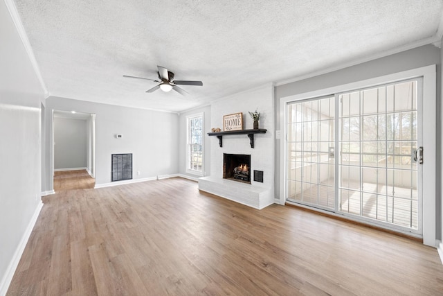 unfurnished living room featuring ceiling fan, a brick fireplace, a textured ceiling, and light wood-type flooring