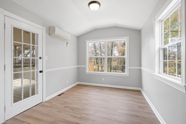 unfurnished dining area featuring a wealth of natural light, lofted ceiling, a wall mounted air conditioner, and light hardwood / wood-style floors