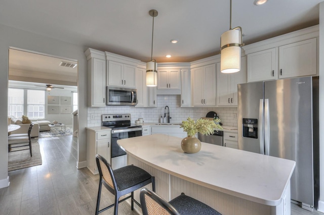 kitchen with sink, hanging light fixtures, backsplash, stainless steel appliances, and white cabinets