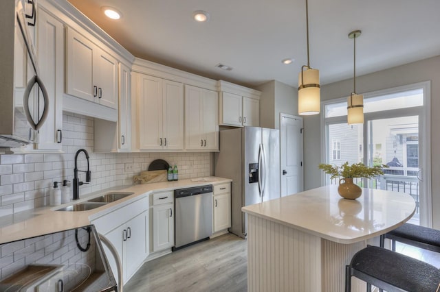 kitchen featuring sink, stainless steel appliances, a kitchen breakfast bar, white cabinets, and decorative light fixtures