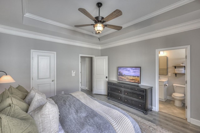 bedroom featuring hardwood / wood-style flooring, ensuite bath, ornamental molding, and a raised ceiling