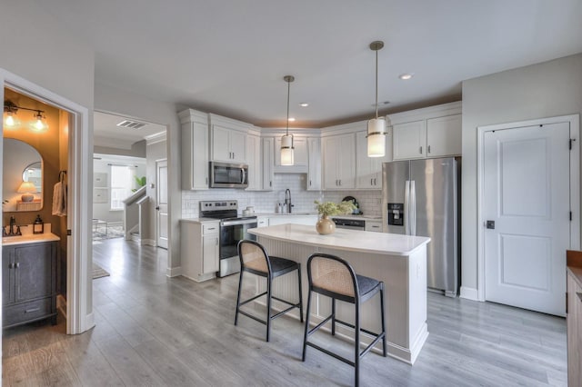 kitchen with a kitchen island, appliances with stainless steel finishes, backsplash, and decorative light fixtures