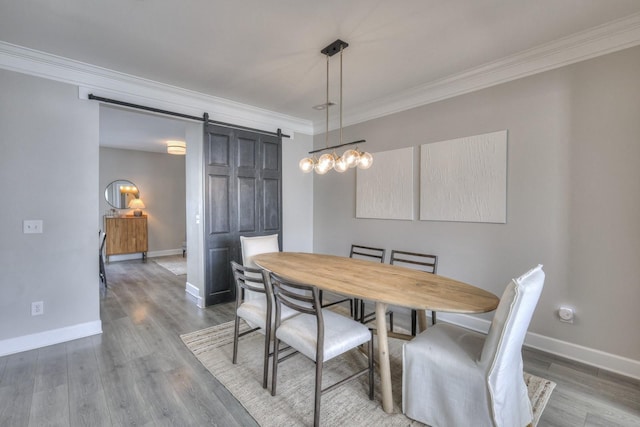 dining room with wood-type flooring, a barn door, and ornamental molding