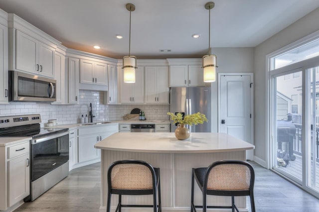 kitchen with appliances with stainless steel finishes, white cabinetry, sink, hanging light fixtures, and a center island