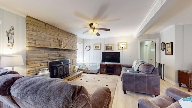 living room featuring ceiling fan, a wood stove, crown molding, and light wood-type flooring