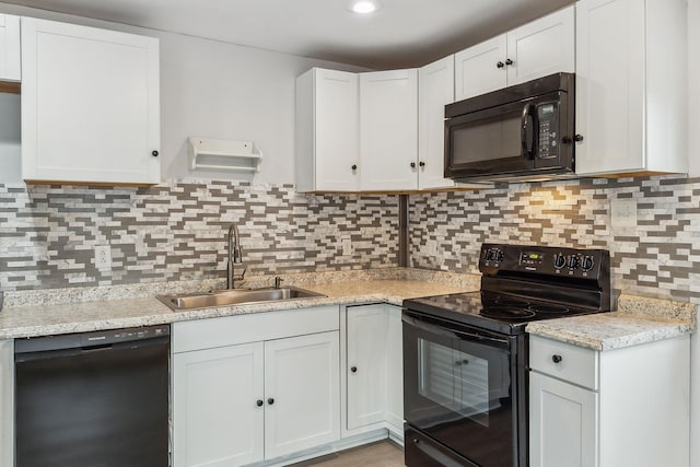 kitchen featuring tasteful backsplash, light stone countertops, white cabinets, black appliances, and sink