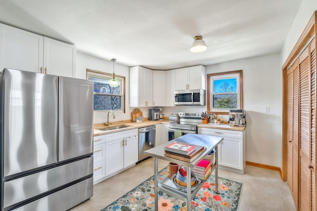 kitchen featuring light tile patterned flooring, sink, pendant lighting, stainless steel appliances, and white cabinets