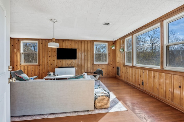 living room featuring wood-type flooring, a healthy amount of sunlight, and wood walls