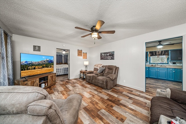 living room featuring sink, ceiling fan, a textured ceiling, and light wood-type flooring