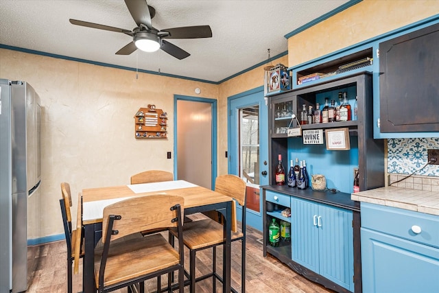 kitchen featuring blue cabinets, crown molding, light wood-type flooring, stainless steel fridge, and tile counters