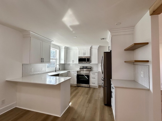 kitchen featuring stainless steel appliances, white cabinetry, light hardwood / wood-style floors, and kitchen peninsula