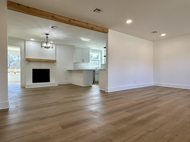 unfurnished living room with sink, light hardwood / wood-style flooring, beam ceiling, a fireplace, and a chandelier