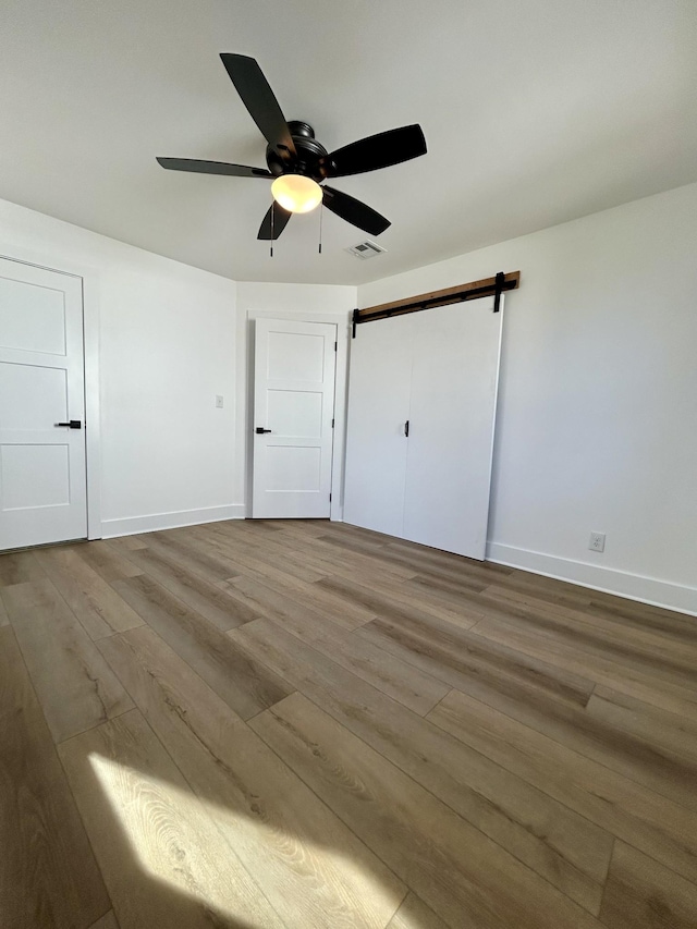 unfurnished bedroom with hardwood / wood-style flooring, a barn door, and ceiling fan