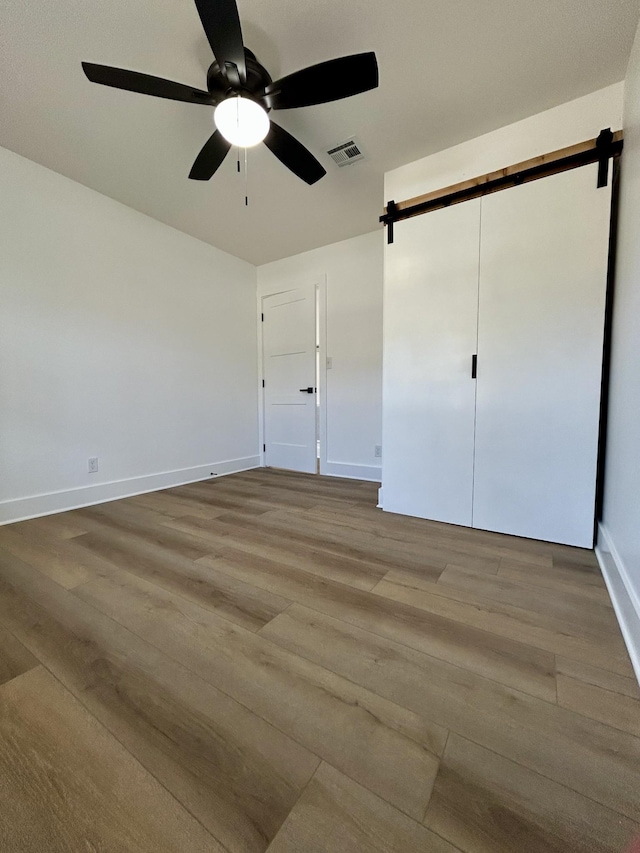 unfurnished bedroom with wood-type flooring, a barn door, and ceiling fan