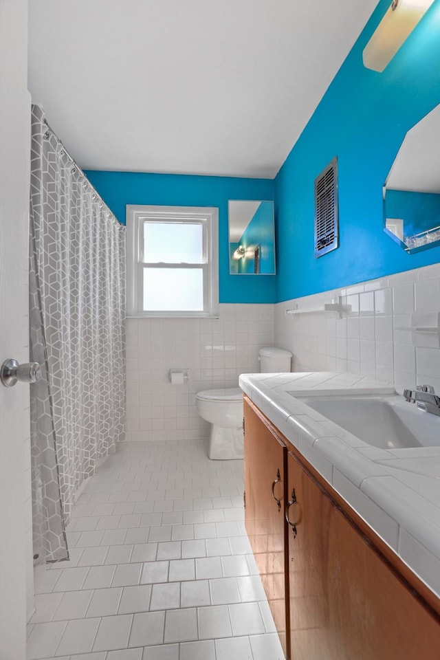 bathroom with tile walls, a shower with shower curtain, vanity, tile patterned floors, and toilet