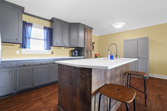 kitchen featuring gray cabinets, sink, a kitchen breakfast bar, dark wood-type flooring, and a center island with sink