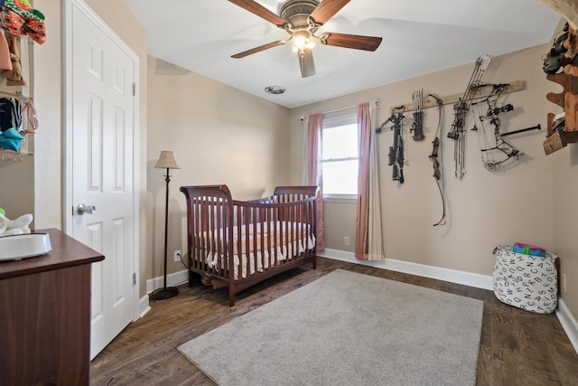 bedroom with a crib, dark hardwood / wood-style floors, and ceiling fan