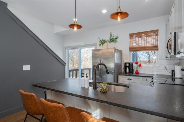 kitchen featuring sink, stainless steel appliances, white cabinets, a kitchen bar, and decorative light fixtures