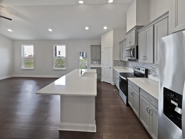 kitchen featuring tasteful backsplash, a center island with sink, appliances with stainless steel finishes, dark hardwood / wood-style floors, and gray cabinets