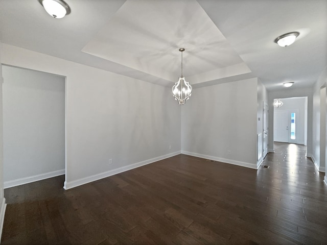 spare room featuring dark hardwood / wood-style floors, a chandelier, and a tray ceiling