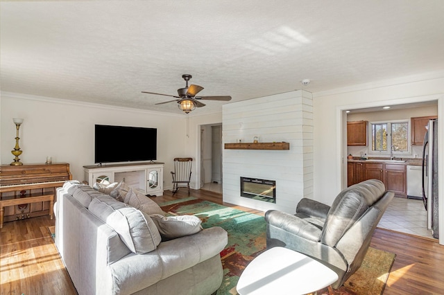 living room with ornamental molding, a large fireplace, sink, and light hardwood / wood-style floors