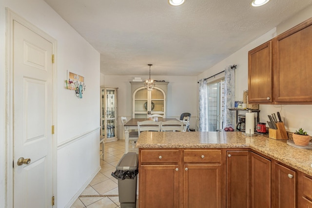 kitchen with light stone counters, decorative light fixtures, a textured ceiling, light tile patterned floors, and kitchen peninsula