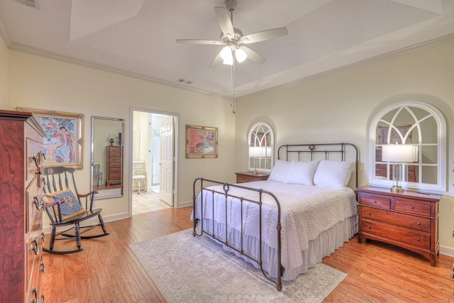 bedroom with crown molding, light hardwood / wood-style flooring, ensuite bath, ceiling fan, and a tray ceiling