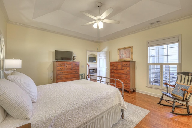 bedroom with light hardwood / wood-style flooring, ornamental molding, a raised ceiling, and ceiling fan