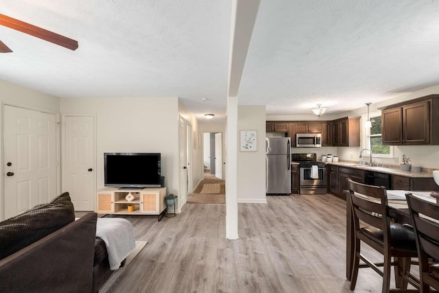 living room with ceiling fan, sink, a textured ceiling, and light wood-type flooring