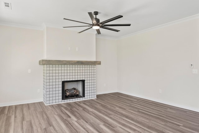 unfurnished living room featuring a brick fireplace, wood-type flooring, ornamental molding, and ceiling fan