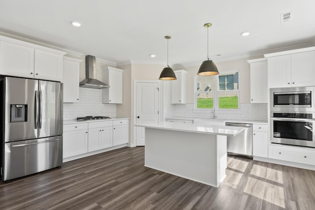 kitchen with hanging light fixtures, stainless steel appliances, white cabinets, a kitchen island, and wall chimney exhaust hood