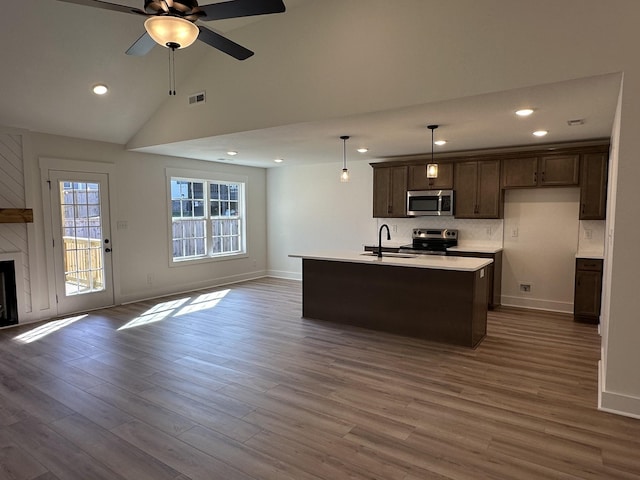 kitchen with pendant lighting, stainless steel appliances, an island with sink, and wood-type flooring