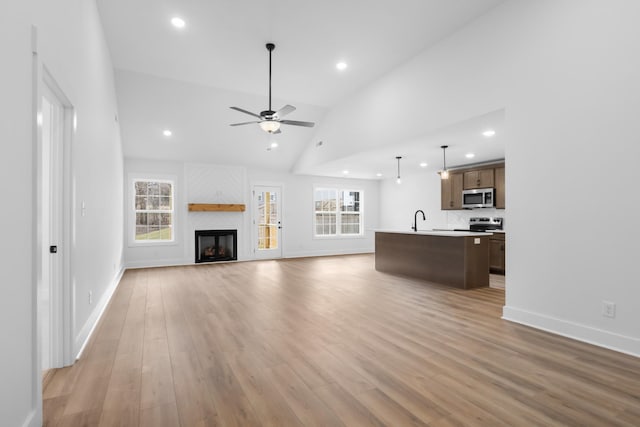 unfurnished living room with sink, vaulted ceiling, light hardwood / wood-style flooring, a large fireplace, and ceiling fan