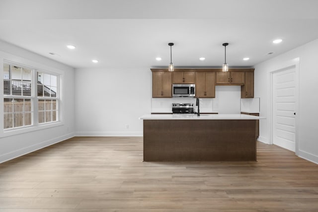 kitchen featuring decorative light fixtures, a center island with sink, light hardwood / wood-style floors, and appliances with stainless steel finishes