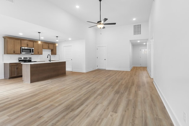 kitchen featuring decorative light fixtures, stainless steel appliances, light hardwood / wood-style floors, and a center island with sink