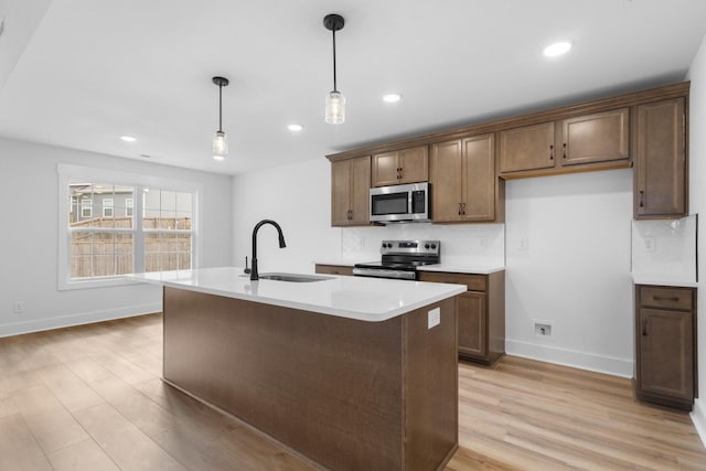 kitchen featuring appliances with stainless steel finishes, pendant lighting, sink, a center island with sink, and light hardwood / wood-style flooring