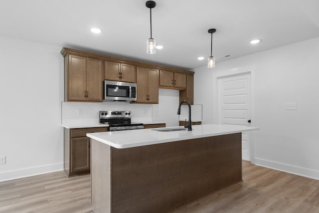 kitchen with pendant lighting, sink, light hardwood / wood-style flooring, a kitchen island with sink, and stainless steel appliances