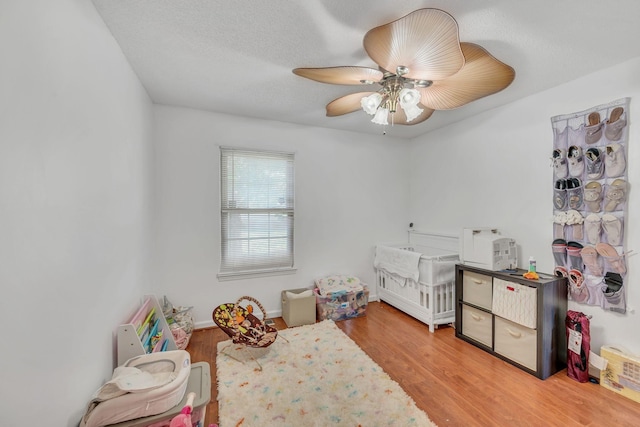 bedroom with a crib, a textured ceiling, ceiling fan, and light hardwood / wood-style flooring